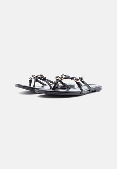 Μαύρα επίπεδα σανδάλια με λεπτές τιράντες και μικρά χρυσά διακοσμητικά σε σχήμα λουλουδιού σε λευκό φόντο.
