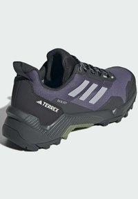 Svart och lila idrottssko med en texturerad ovandel, reflektiva detaljer, gummisula och ett robust mönster för bra grepp.