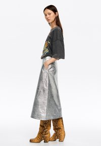 Metalen zilveren lange rok met zijzakken, gecombineerd met een grafisch charcoal t-shirt en bruine slangenprint kniehoog laarzen.