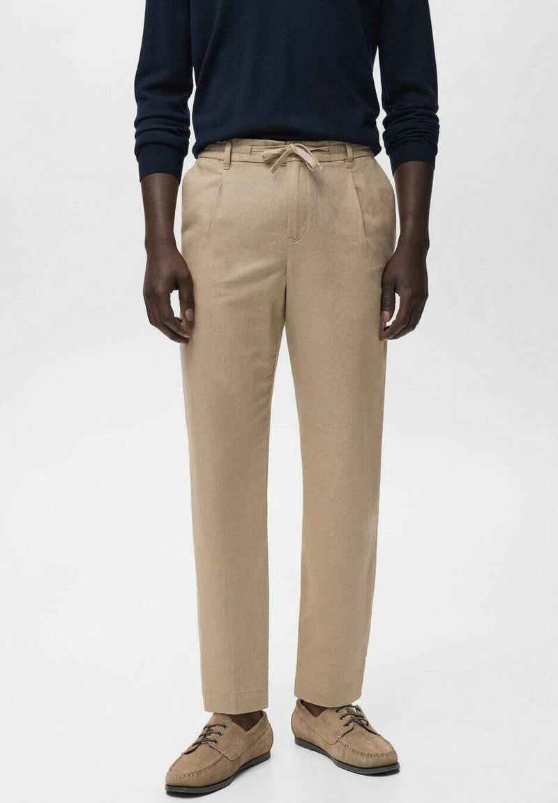 Pantalons beiges fuselés en tissu léger, avec une taille à cordon et deux poches avant. Associés à des chaussures à lacets marron clair.