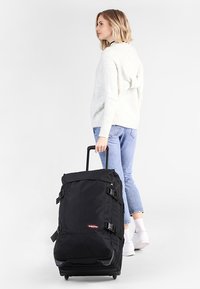 Zaino con ruote nere, dal design strutturato, con spallacci regolabili e fibbie. Realizzato in tessuto resistente, presenta una base che scorre agevolmente.