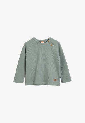 Camiseta de bebé de manga larga con canalé en verde suave, con dos botones en el hombro y un pequeño parche de cuero circular cerca del dobladillo.