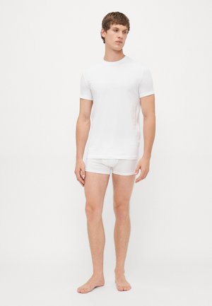 Weißes Baumwoll-T-Shirt mit kurzen Ärmeln, kombiniert mit weißen Unterhosen. Die Passform ist eng und der Stoff scheint glatt und leicht zu sein.