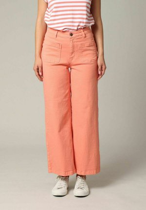 Jeans larges pêche avec deux poches avant, passants de ceinture et une légère texture. Portés avec une chemise rayée et des baskets blanches.