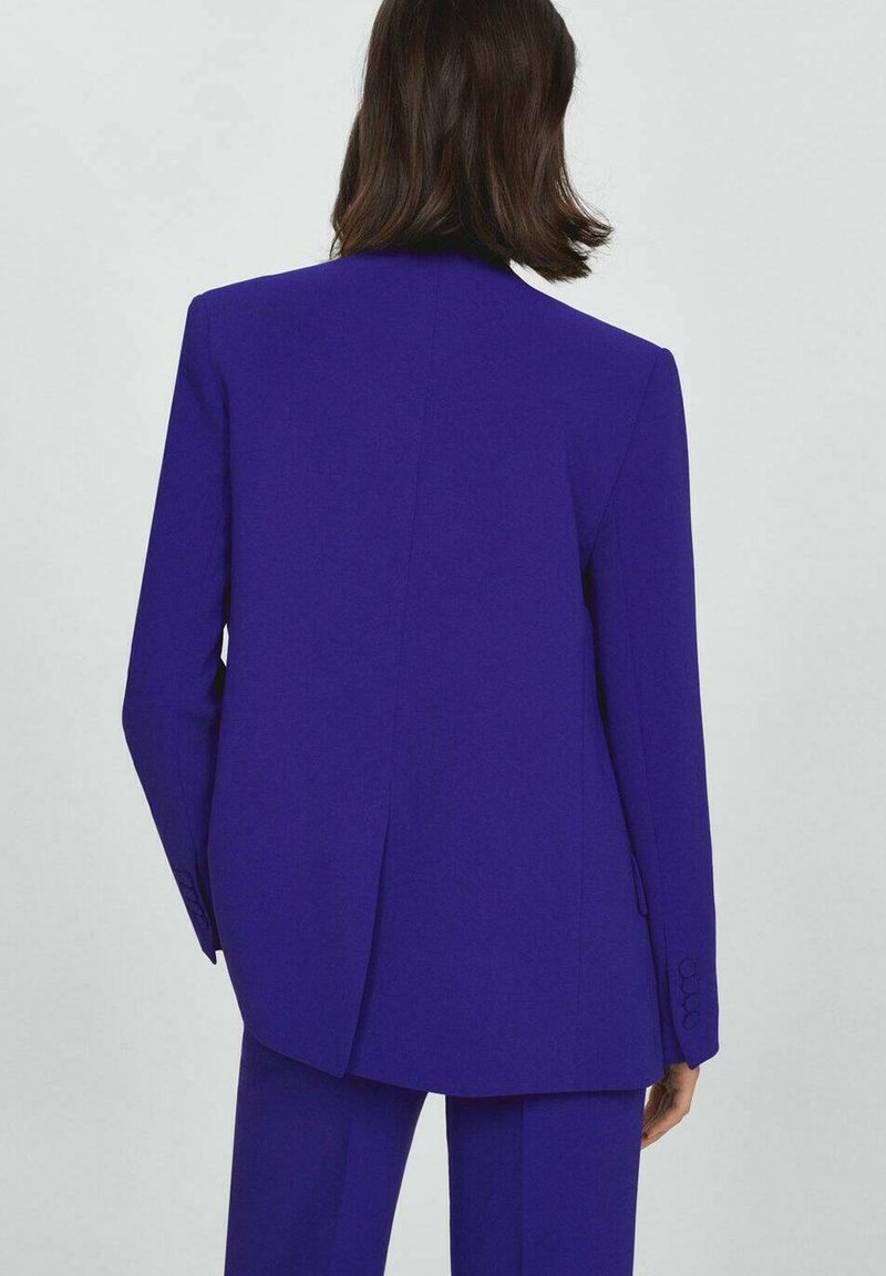 Blazer viola vivace con colletto a revers, spacco singolo sul retro e dettagli con maniche abbottonate. Tessuto liscio e vestibilità su misura.