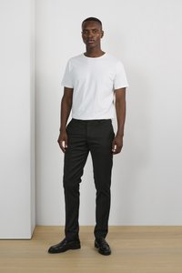T-shirt en coton blanc associée à un pantalon noir slim. Chaussures en cuir noires. Design minimaliste avec des textures lisses et des couleurs neutres.