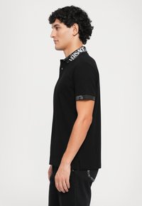 Sort polo skjorte med en mønstret sort krave med logo, korte ærmer med kontrastkanter og sideslidser for komfort.