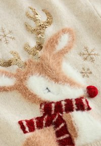 Brun og hvid strikket rensdyr design med gyldne paliet-antler, rød pom-pom næse og et stribet rødt tørklæde på en cremet baggrund.