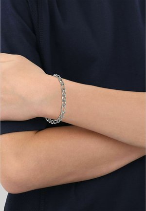 Arm verschränkt mit einem silbernen Gliederarmband vor einem dunklen kurzärmeligen Shirt.