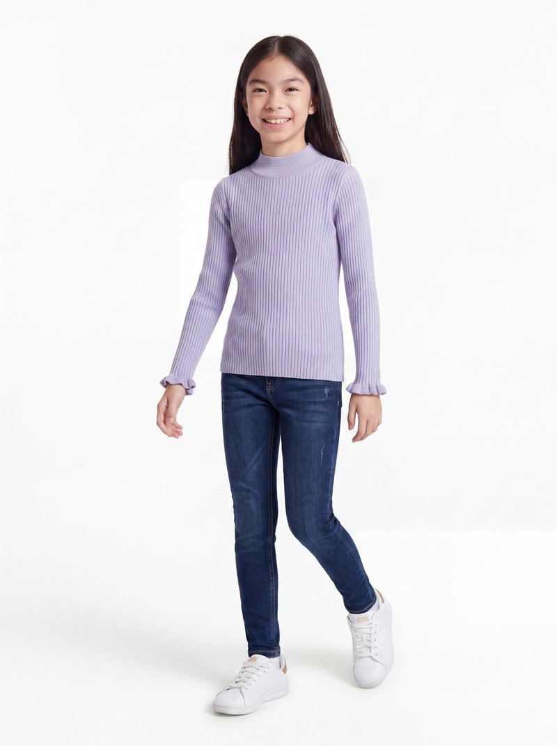 Fille souriante aux longs cheveux foncés marchant, portant un pull léger violet clair côtelé, un jean bleu foncé et des baskets blanches sur fond blanc.