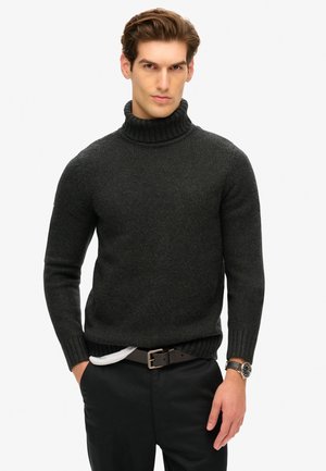 Maglione a collo alto grigio scuro, texture a costine, design aderente. Indossato con pantaloni neri e una cintura marrone. Accentuato da un orologio al polso.