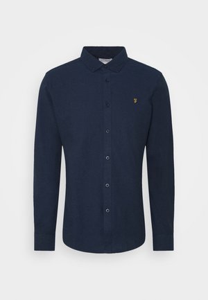 Navy blue button-up shirt with long sleeves, collar, and small yellow embroidered logo on left chest. Smooth fabric with structured fit.