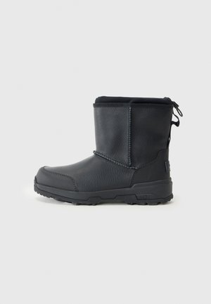 Bottines noires en cuir lisse et en caoutchouc avec une surface texturée, bout rond, languette et semelle extérieure épaisse à crampons.