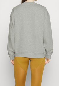 Kvinna sedd bakifrån iförd en lös grå sweatshirt och senapsgula leggings med böjda sömmar.