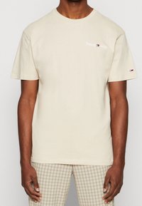 Beige cotton t-shirt with short sleeves and a round neckline, featuring a small white embroidered "Tommy Jeans" logo on the chest.