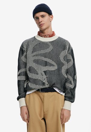 Strikket sweater med et stribet mønster i sort og creme, rund halsudskæring, ribbede manchetter og en løs pasform, parret med khaki bukser.