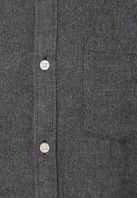 Chemise boutonnée gris foncé en tissu texturé, dotée d'une poche plaquée et de boutons de couleur claire avec quatre trous.