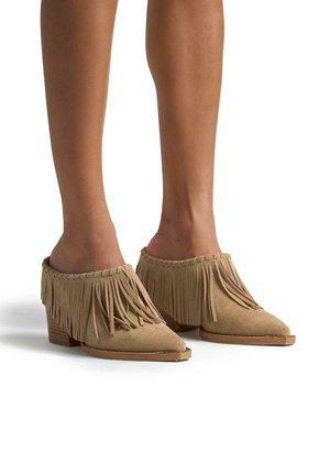 Tan suède hoge muiltjes met franjes, spitse neus en een gestructureerde achterkant. Heeft een lage blokhak en decoratieve stiksels aan de rand.