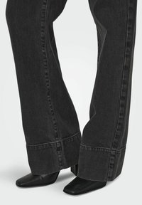 Vaqueros de denim negros de pierna ancha con un dobladillo deshilachado, combinados con zapatos de tacón alto de punta cuadrada en negro. La tela tiene una textura suave.
