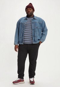 Denim jacket in blue with button closures, striped t-shirt in navy and white, dark gray pants, and maroon sneakers with white accents.