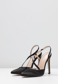 Svarta satin högklackade slingback-skor med spetsiga tår, korsade remmar och en tunn stilettklack. Slät textur och minimala detaljer.