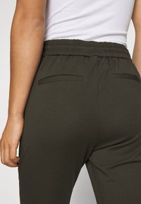 Donkergroene joggingsbroeken met een elastische tailleband, voorzien van twee achterzakken en een gladde, rekbare stof. De zijnaden zijn discreet.
