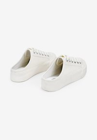 Scarpe da ginnastica bianche in tela con un design slip-on, suola piatta in gomma e occhielli argentati per i lacci, caratterizzate da una texture minimalista e liscia.