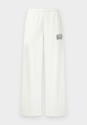 Valged laia säärega dressipüksid, millel on elastne vöökoht ja must GAP logo vasaku reie ülemisel osal.