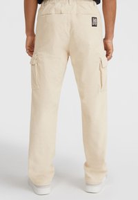 Beige corduroy cargo-housut, joissa on joustava vyötärö, sivutaskut ja logo-patch takana. Silkkinen rakenne, suorat lahkeet.