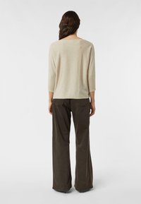 Beżowa, błyszcząca bluzka z rękawami do łokcia, zestawiona z ciemnymi, szerokimi spodniami. Gładka tekstura; dopasowuje się do kształtu sylwetki od tyłu.