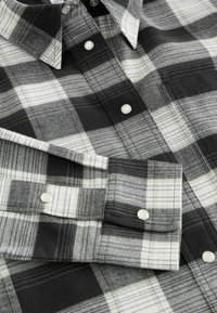Black and white checkered flannel shirt with a button-down collar, structured fabric, and contrasting white buttons. Features horizontal and vertical lines.