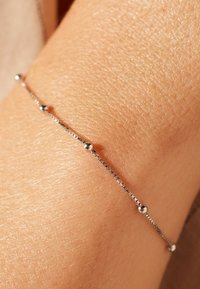 Silver chain bracelet featuring small round beads, with a delicate, thin design and polished texture, shown on tanned skin.