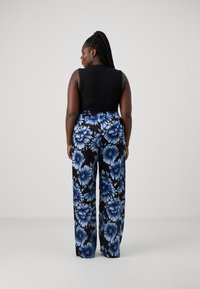 Svart ermeløs topp kombinert med løse, svarte bukser med blomsterprint som har store blå blomster på svart bakgrunn. Elastisk midjebånd.