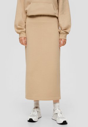 Jupe midi beige en tissu doux, dotée d'une taille ajustée et d'une silhouette droite, associée à des baskets blanches et des chaussettes légères.