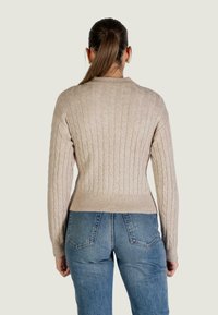 Beige gebreide trui met kabelstructuur, geribbelde zoom en manchetten, gecombineerd met blauwe spijkerbroek. Achteraanzicht, laat de eenvoud van het ontwerp zien.