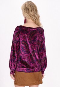 Lila Bluse mit Paisleymuster, langen, puffärmeln und einem weiten Ausschnitt, kombiniert mit einem Rock aus braunem Wildleder. Glatte Textur, lebhafte Farben.