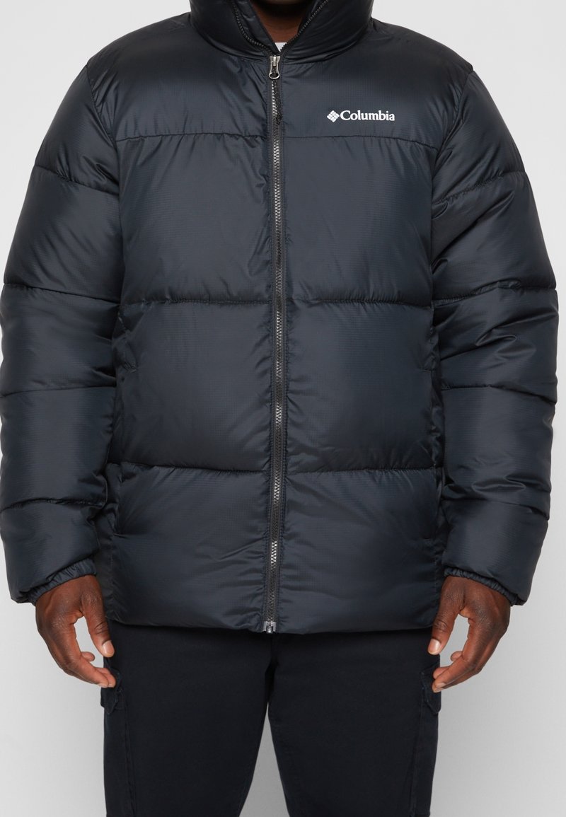 Černá zateplená prošívaná bunda s vysokým límcem, zapínáním na zip a logem Columbia na hrudi. Má prošívaný design a hladký povrch.