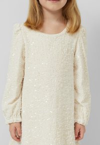 Crèmekleurige jurk met lange, geplooide mouwen, bedekt met kleine pailletten, voorzien van een ronde halslijn en geplooide manchetten.