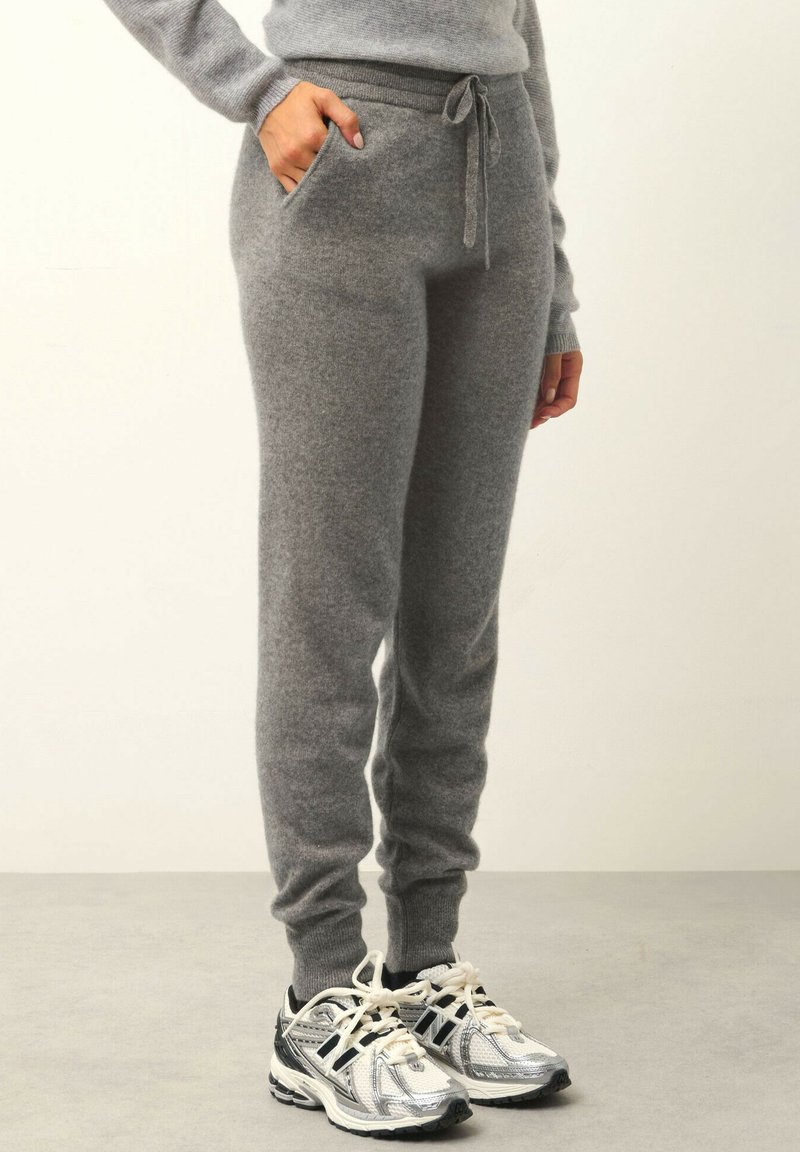 Grå stickade sweatpants med dragsko i midjan, sidofickor och ribbade muddar; bärs med silverfärgade träningsskor. Mjuk textur.
