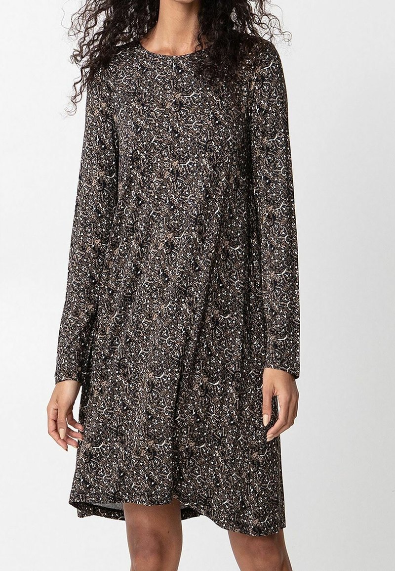 Femme portant une robe à manches longues, longueur genou, avec un motif floral et abstrait complexe en noir et beige.