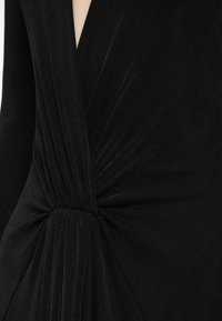 Black dress featuring a deep V-neck, textured fabric, and draped detailing with a knotted accent at the waist. Smooth and form-fitting.