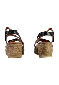 Des sandales en cuir noir à plateforme présentent des lanières entrecroisées et une semelle en jute tressé avec un design empilé. La vue arrière montre des brides de cheville ajustables.