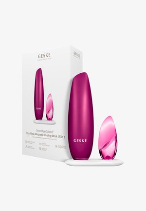 Lilla og pink slanke skønhedsapparater på en hvid base, ved siden af emballage mærket "Touchless Magnetic Peeling Mask 5 i 1" af GESKE.