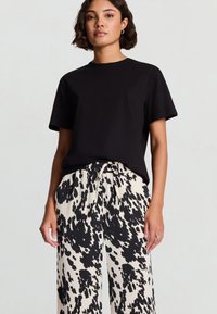 Maglietta nera a maniche corte abbinata a pantaloni a gamba larga crema e neri a macchie, con vita elasticizzata e coulisse.