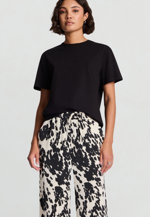 Maglietta nera a maniche corte abbinata a pantaloni a gamba larga crema e neri a macchie, con vita elasticizzata e coulisse.