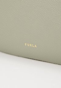 Superficie della borsa in pelle verde con una finitura testurizzata. Presenta un logo "FURLA" in rilievo dorato. Design semplice senza hardware o accenti aggiuntivi.