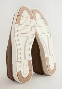 Zapatos de ante marrón con una textura suave. Suelas de goma blanca con ranuras horizontales y acentos beige. Diseñados para un uso casual.
