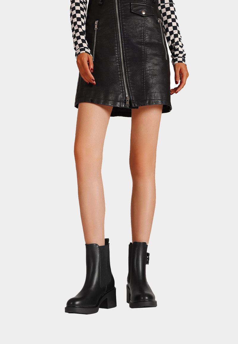 Stivali neri alla caviglia con tacco robusto, texture in pelle liscia, pannelli elastici laterali e una linguetta posteriore per un facile indossamento.