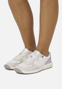 Baskets légères en beige et blanc, avec une tige en mesh et daim, des lacets plats et une semelle en caoutchouc. Détails en violet pastel.