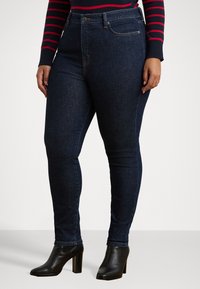 Mørkeblå høyhalsede skinny jeans laget av denim, med subtile sømmer, fem lomme-design og klassisk liv. Svart hælhøyde ankelstøvler.